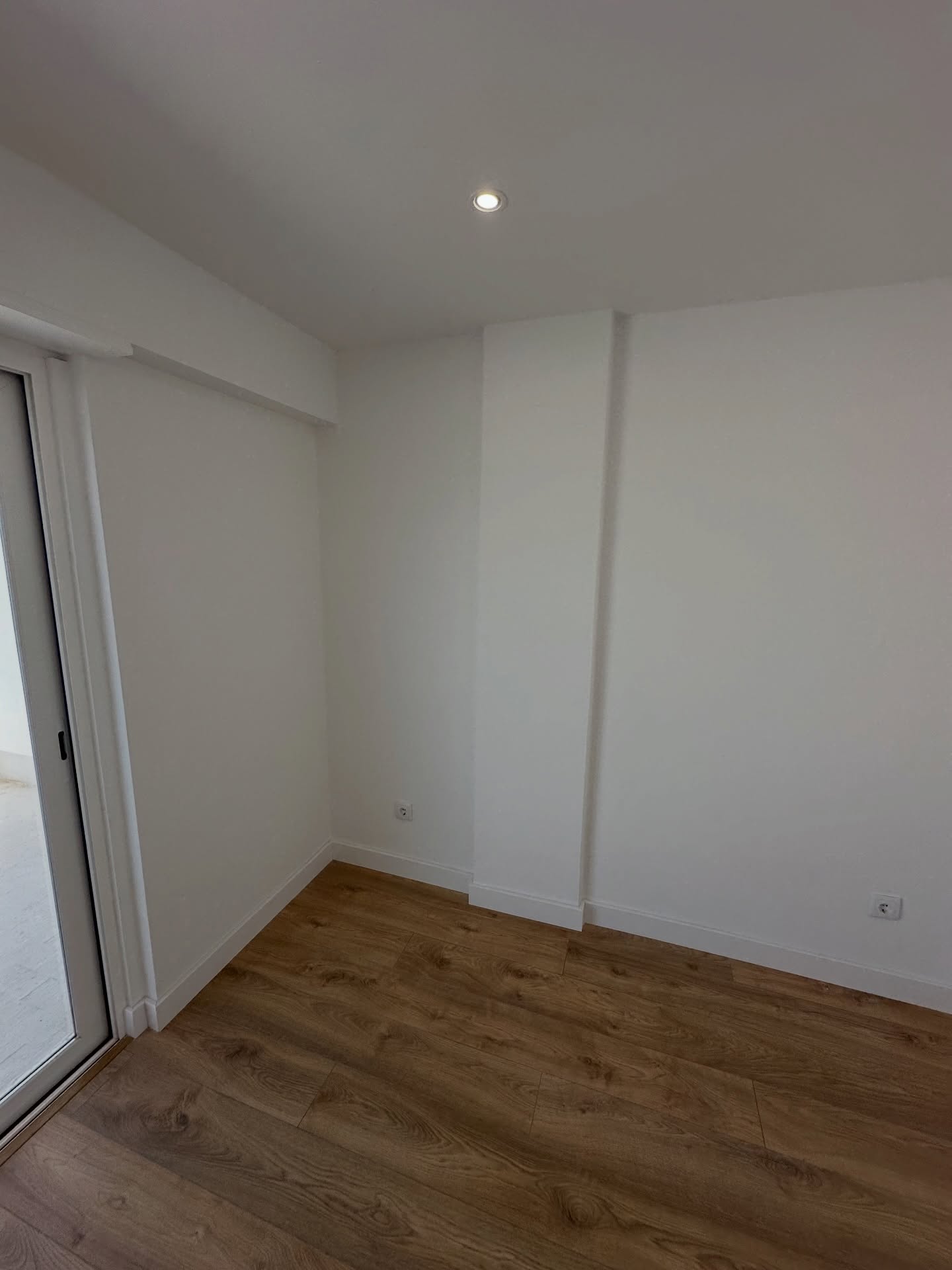 Quarto pintado de branco com pavimento novo em madeira e acesso à varanda