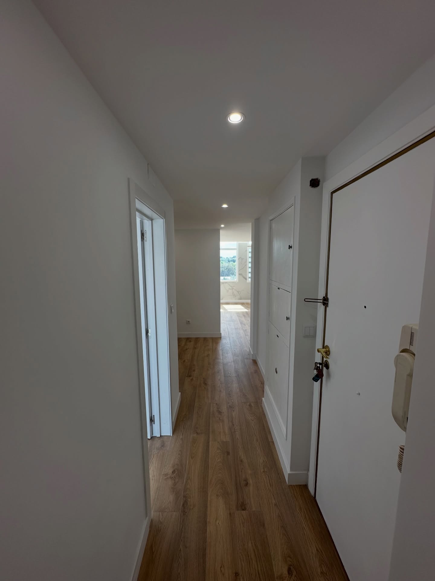 Corredor de apartamento remodelado com pavimento em madeira e iluminação embutida
