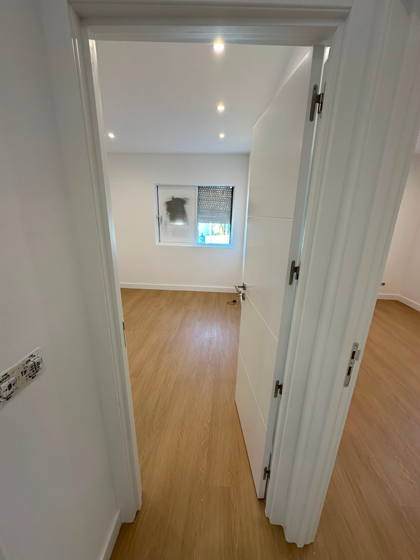 Quarto remodelado visto do corredor com pavimento em madeira e porta lacada