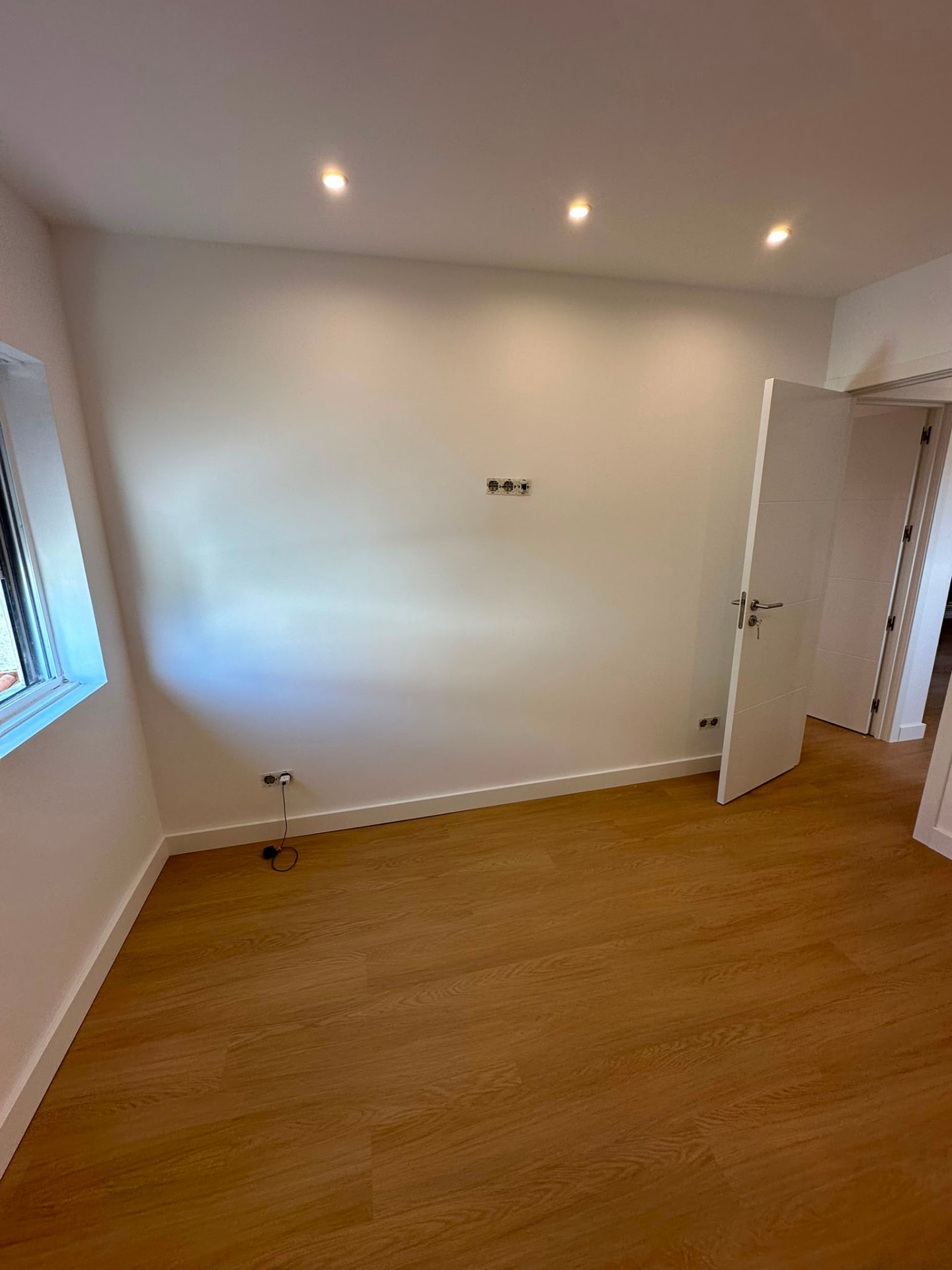 Quarto amplo com iluminação embutida, pintura branca e pavimento em madeira