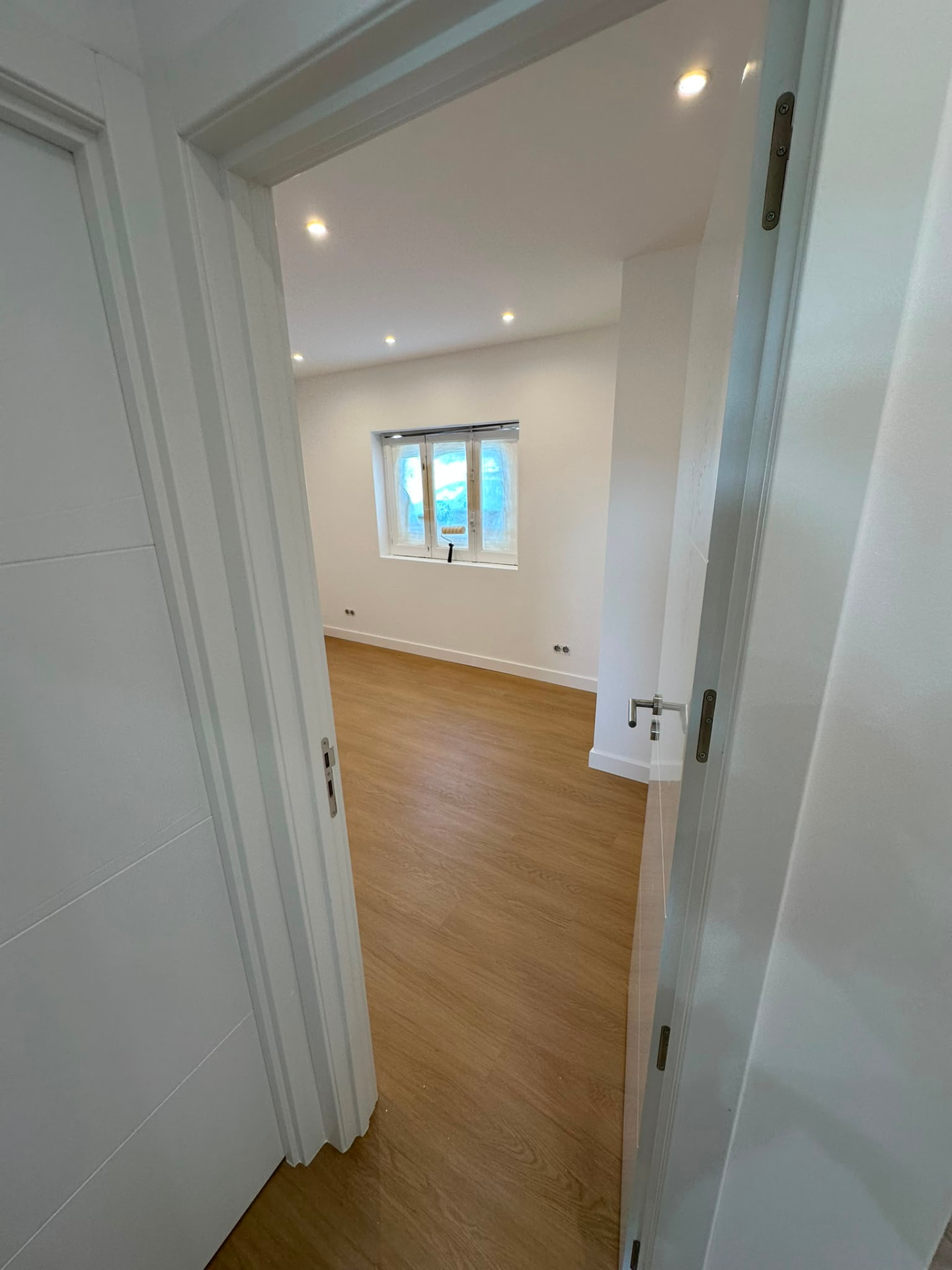 Quarto remodelado visto do corredor com porta lacada branca e iluminação embutida