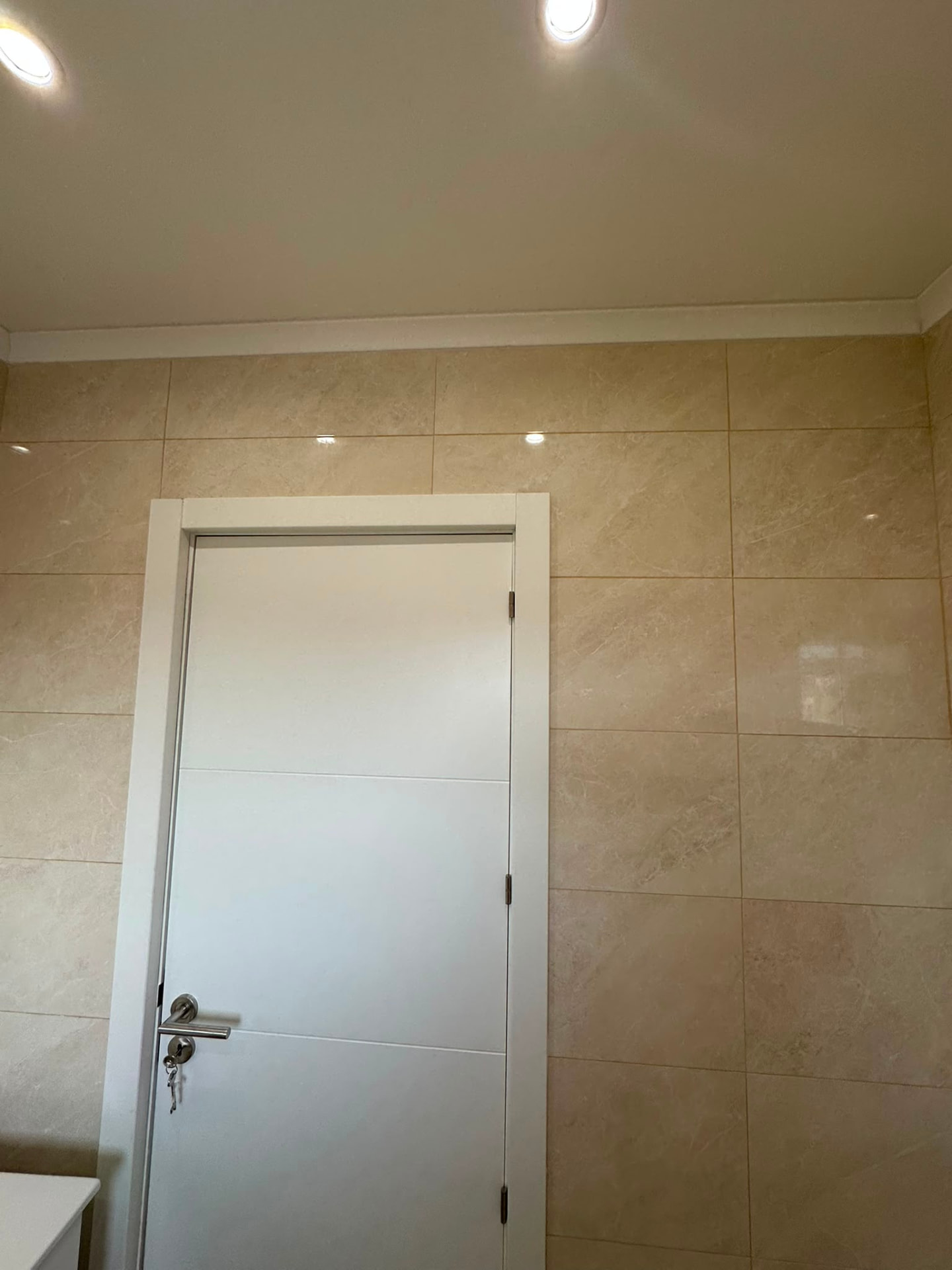 Casa de banho revestida a ladrilho efeito mármore com porta branca e iluminação embutida